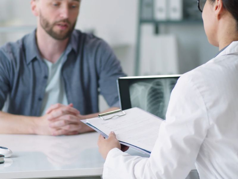 Muškarac na pregledu kod doktorke, pored nje rengen snimak pluća i ona drži papirologiju u rukama